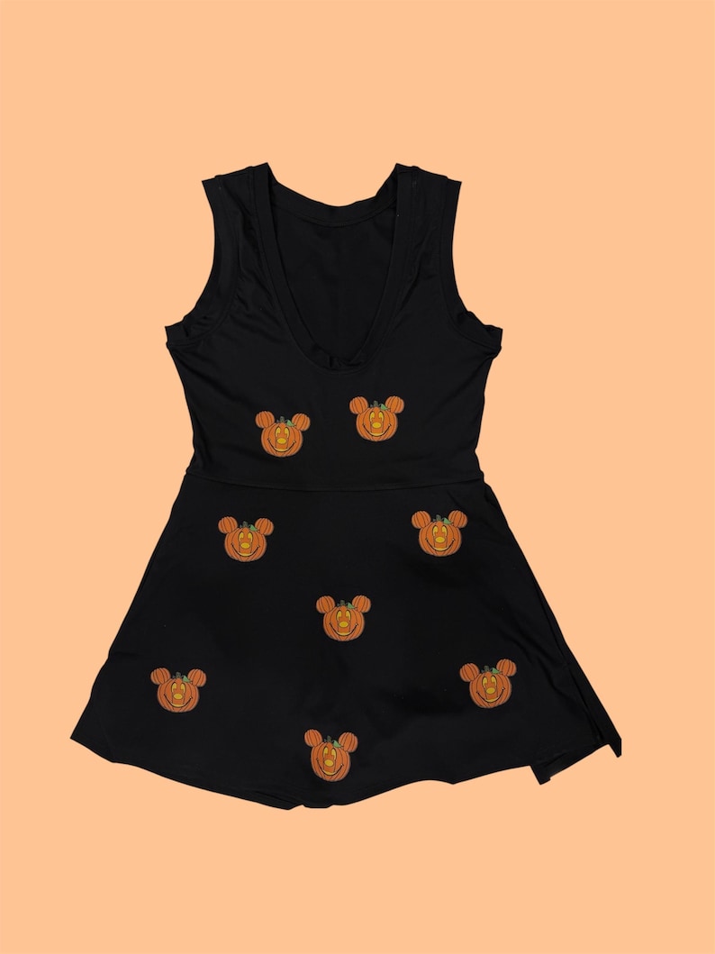May include: Black sleeveless dress with a V-neckline. The dress features embroidered orange pumpkin designs with mouse ears. The dress has a fitted bodice and a flared skirt, perfect for Halloween or themed events.
