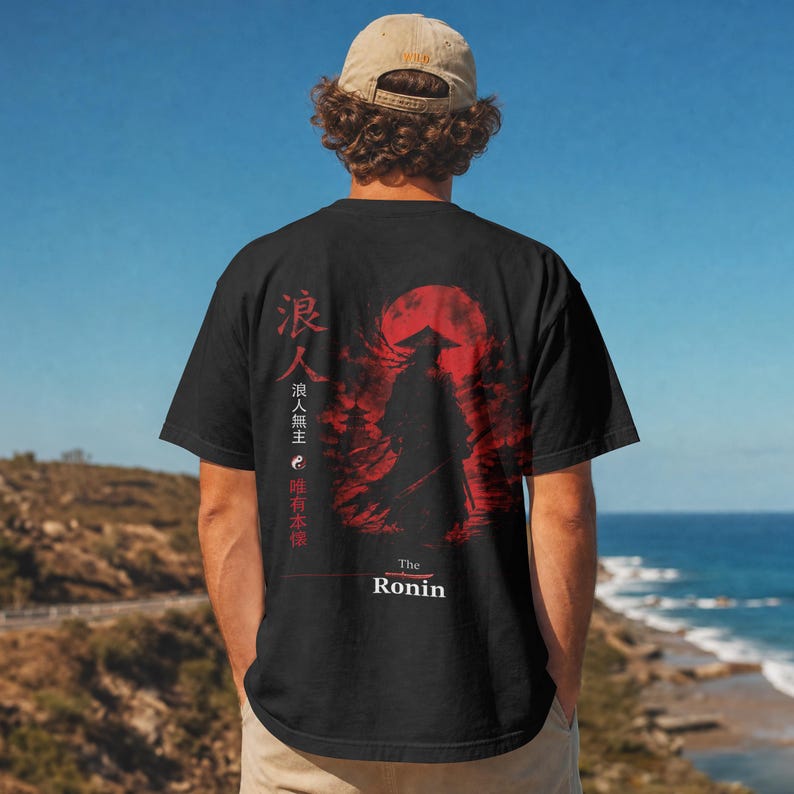May include: A black t-shirt featuring a red graphic of a silhouetted samurai standing before a large red moon. The design includes Japanese kanji characters, a yin-yang symbol, and the text "The Ronin" printed in white at the bottom of the graphic.