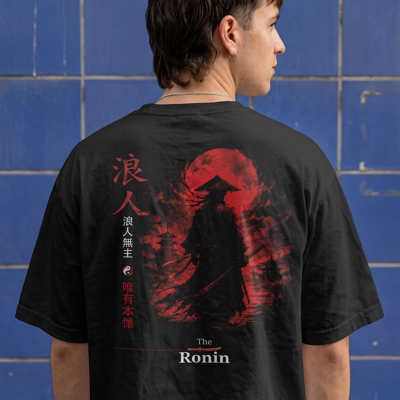 May include: A black t-shirt featuring a graphic print on the back. The design displays a silhouette of a warrior in a conical hat against a large red sun, with Japanese kanji characters, a yin-yang symbol, and the text The Ronin at the bottom.