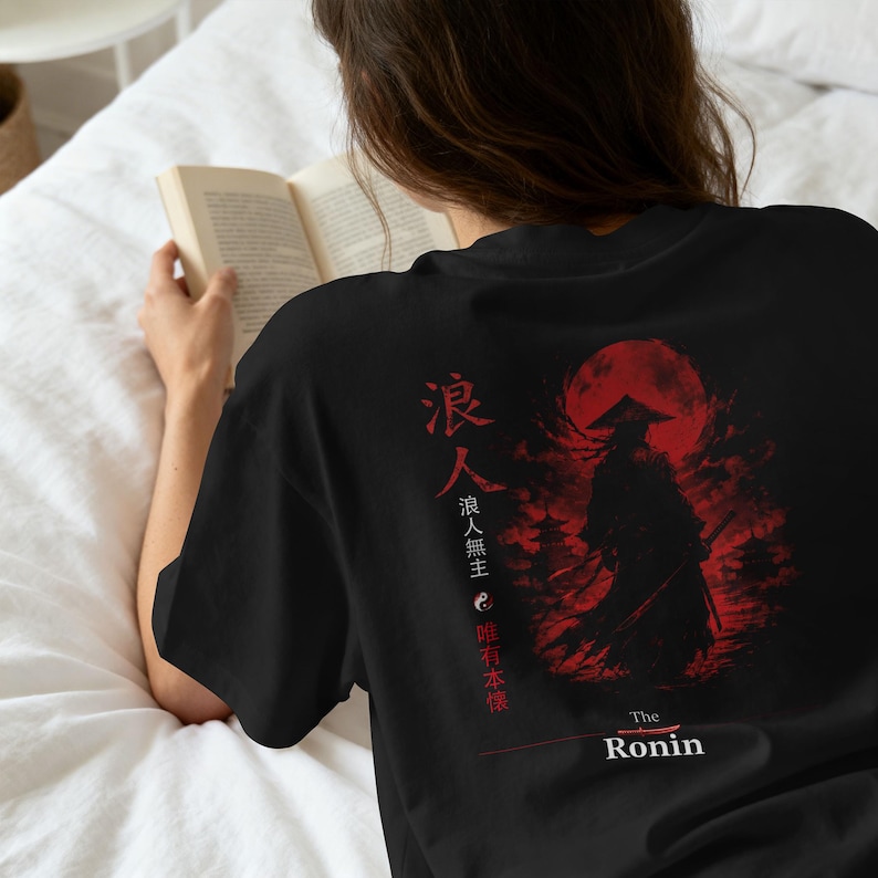 May include: A black t-shirt featuring a red graphic print on the back. The design depicts a silhouetted figure in a conical hat against a large red moon, accompanied by Japanese kanji characters, a yin-yang symbol, and the text The Ronin.