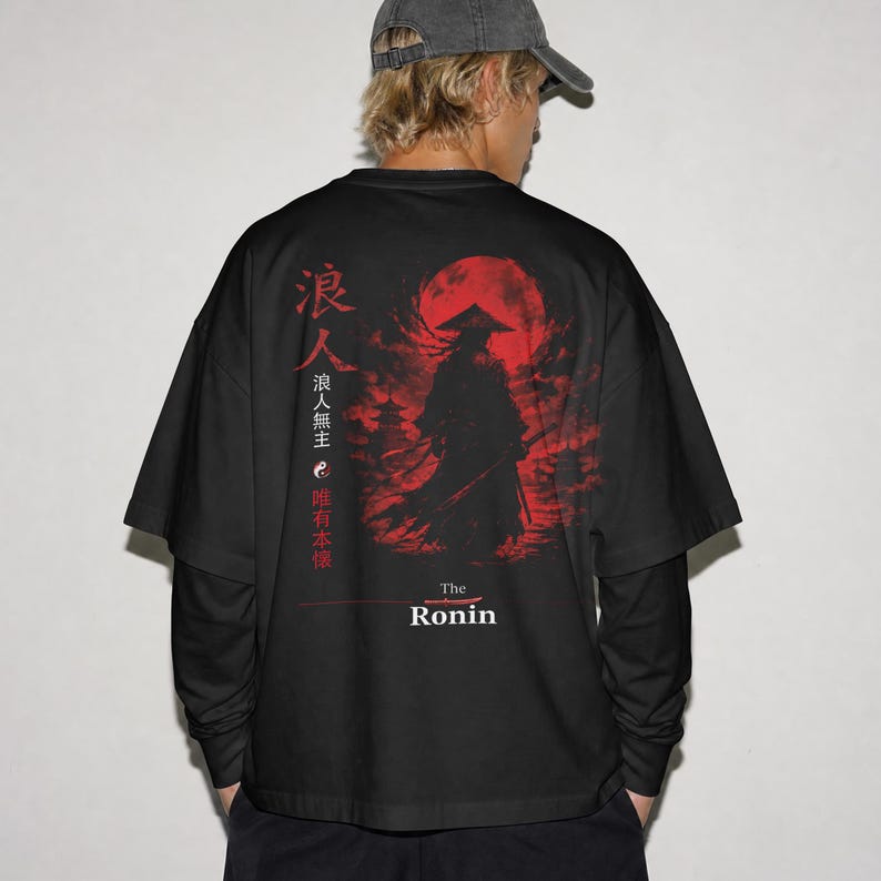May include: A black long-sleeve t-shirt featuring a graphic print on the back. The design displays a silhouette of a samurai in a conical hat against a large red moon, with Japanese kanji characters, a yin-yang symbol, and the text The Ronin.