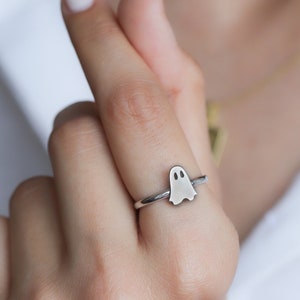 May include: A silver ring with a ghost design. The ghost is a simple outline with two small circles for eyes.