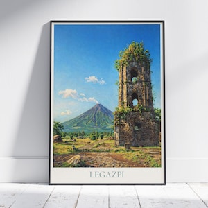May include: Framed art print featuring a scenic landscape of Legazpi, Philippines. The image showcases a weathered stone bell tower with arched openings, lush greenery, and a distant volcano under a bright blue sky. The word "LEGAZPI" is printed at the bottom.