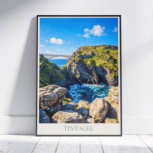 Puede incluir: Impresión enmarcada de un paisaje costero con un puente que cruza una ensenada rocosa. La imagen muestra un cielo azul, acantilados verdes y agua turquesa. La palabra "Tintagel" está impresa en la parte inferior.