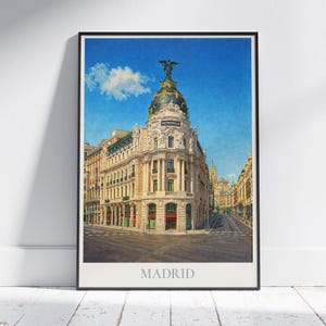 Może przedstawiać: Oprawiony wydruk przedstawiający akwarelę budynku Metropolis w Madrycie, Hiszpania. Grafika ukazuje bogatą architekturę budynku na tle błękitnego nieba. Słowo "MADRID" jest wydrukowane na dole.