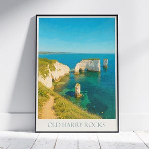 Op de afbeelding: Een ingelijste print met een kustlandschap met de tekst "OLD HARRY ROCKS" onderaan. De afbeelding toont witte rotsformaties in turquoise water onder een heldere blauwe lucht. Groene vegetatie omzoomt de kliffen.