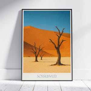 Könnte beinhalten: Ein gerahmter Kunstdruck mit einer Wüstenlandschaft mit orangefarbenen Sanddünen unter einem klaren blauen Himmel. Drei kahle Bäume stehen im Vordergrund. Der Text "SOSSUSVLEI" ist unten auf dem Druck abgebildet.