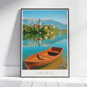 Può includere: Una stampa incorniciata del lago di Bled, in Slovenia, con una barca a remi in legno su acqua turchese. L'immagine mostra una chiesa su un'isola, con montagne sullo sfondo. Il testo "LAKE BLED" è in basso nella stampa.