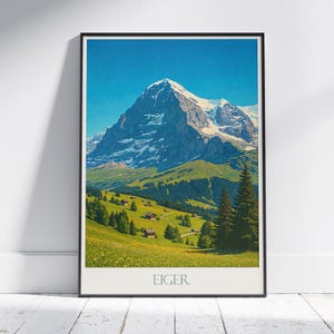 Puede incluir: Un póster enmarcado con una vista panorámica de la montaña Eiger en Suiza. La imagen muestra un pico nevado, colinas verdes y pequeños edificios bajo un cielo azul claro. La palabra "EIGER" está impresa en la parte inferior.