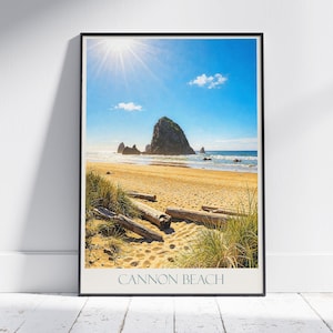 May include: Framed print of Cannon Beach, Oregon, showing a sunny sky and a large rock formation in the sea. The beach has golden sand, green grass, and driftwood logs. The text "CANNON BEACH" is at the bottom.