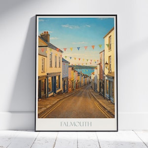 May include: A framed print of Falmouth, featuring a street scene with colorful buildings and a view of the water. The artwork includes a road lined with buildings, a blue sky, and strings of triangular flags. The word "FALMOUTH" is printed at the bottom.