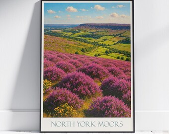Może przedstawiać: Oprawiony wydruk przedstawiający krajobraz North York Moors. Obraz przedstawia wzgórza pokryte fioletowym wrzosem, zielone pola i krętą drogę. Niebo jest niebieskie z chmurami. Tekst "NORTH YORK MOORS" znajduje się na dole.