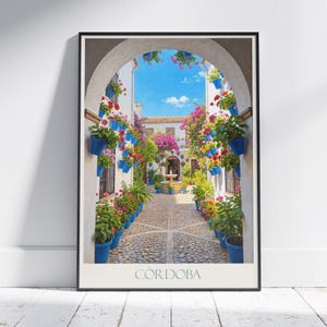 May include: Framed print depicting a courtyard scene in Cordoba, Spain. A cobblestone path is flanked by blue flower pots brimming with colourful flowers. An archway frames the view of the courtyard, with a fountain and buildings in the background. The word "CORDOBA" is printed at the bottom.