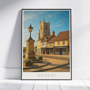 May include: A framed print depicting Halstead, England, with a church, clock tower, and traditional buildings. A vintage street lamp and flowerbeds are in the foreground. The print is in a black frame, with the word "HALSTEAD" at the bottom.