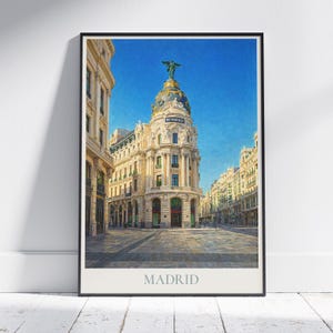 May include: A framed print featuring a detailed watercolor painting of the Metropolis building in Madrid, Spain. The image showcases the building's ornate architecture under a clear blue sky, with the word "MADRID" at the bottom.