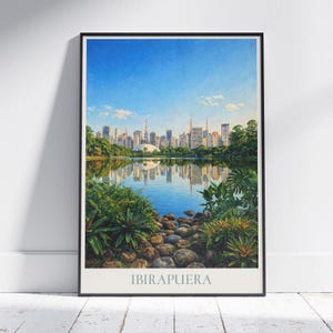 May include: A framed art print featuring a scenic view of Ibirapuera Park in São Paulo, Brazil. The artwork depicts a serene lake reflecting the city skyline under a clear blue sky. Lush greenery and rocks frame the water, with the park's name at the bottom.