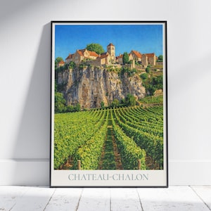 Op de afbeelding: Ingelijste print van Chateau-Chalon, een Frans dorp. De afbeelding toont een wijngaard op de voorgrond, een rotsachtige klif en gebouwen met rode pannendaken onder een blauwe lucht. De tekst "CHATEAU-CHALON" staat onderaan.