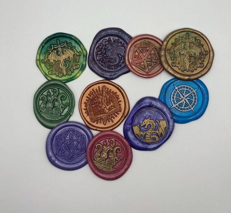 May include: A collection of colorful wax seals with various designs, including a dragon, a compass rose, a ship, and a die. The seals are in shades of green, blue, purple, gold, and red, and are arranged on a white surface.