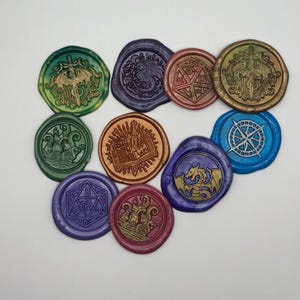 May include: A collection of colorful wax seals with various designs, including a dragon, a compass rose, a ship, and a die. The seals are in shades of green, blue, purple, gold, and red. These decorative seals are ideal for adding a unique touch to letters or crafts.