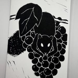 May include: Black and white linocut print of a squirrel perched on a bunch of grapes. The squirrel is depicted in silhouette, holding a grape. A large leaf and vine are also visible.