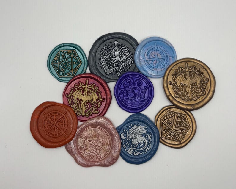 May include: A collection of colorful wax seals with various designs, including a compass, a dragon, a d20 die, and a sword and shield. The seals are in shades of blue, red, gold, and purple, and are arranged on a white surface.