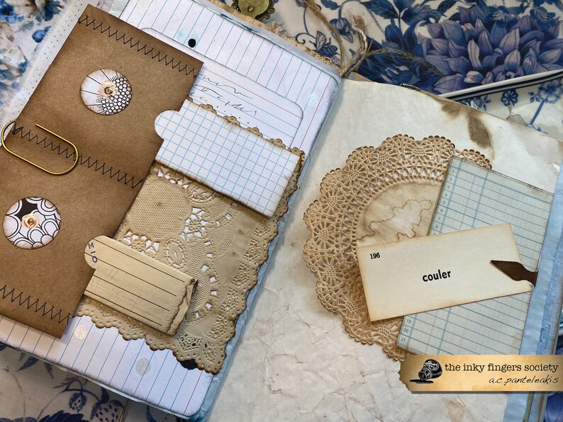 May include: A vintage journal with brown paper covers, a paper doily, and a tag that says "couler". The journal has a worn and aged look, with visible stitching and a paper clip.