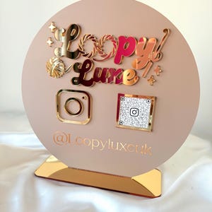 May include: A circular beige acrylic sign featuring the gold mirrored text Loopy Luxe, a gold yarn ball icon, and star accents. Below are a gold Instagram logo, a square QR code, and the text @Loopyluxcuk, all mounted on a gold mirrored base.