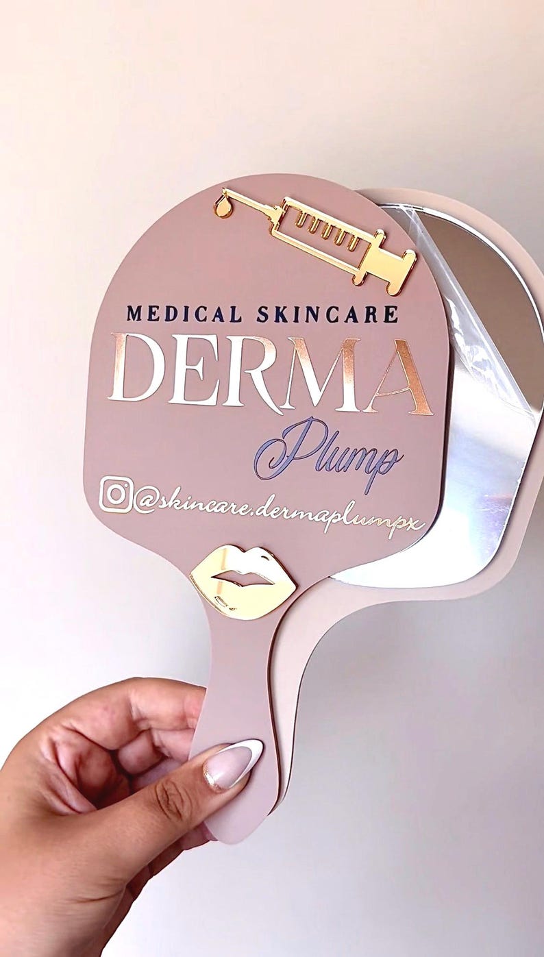 May include: A dusty rose handheld mirror featuring a gold syringe icon at the top and a gold lip icon on the handle. The text reads MEDICAL SKINCARE DERMA Plump with an Instagram icon and the handle @skincare.dermaplumpx in white lettering.