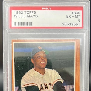 Peut inclure: Une carte de baseball Topps de 1962 représentant Willie Mays des Giants de San Francisco. La carte est en excellent état et est classée EX-MT 6 par PSA. La carte montre Mays dans une position de frappe, portant un uniforme blanc et orange avec le logo de l'équipe sur le devant. La carte est entourée d'une bordure blanche et a un fond rouge et blanc.