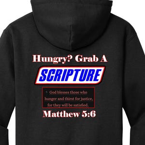 May include: Black hooded sweatshirt with the text "Hungry? Grab A SCRIPTURE" in white, red, and blue. Below the text is a Bible verse from Matthew 5:6 in a red box.