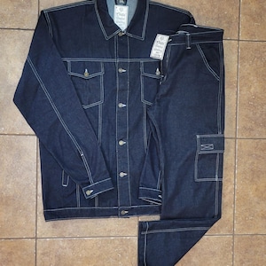 May include: A dark blue denim jacket and matching pants set. The jacket has a button-up front, two chest pockets, and white stitching. The pants have a cargo pocket and white stitching. The set is laid out on a tiled surface.