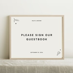 Puede incluir: Un cartel blanco en un marco de madera claro con el texto "Riley & Archer" y "Por favor, firme nuestro libro de visitas" con la fecha "18 de septiembre de 2026".