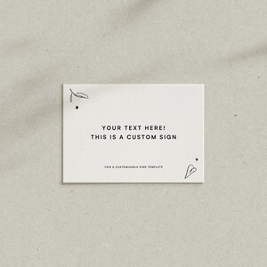 Puede incluir: Un letrero rectangular blanco con el texto "YOUR TEXT HERE! THIS IS A CUSTOM SIGN" en negro. El letrero tiene garabatos minimalistas de hojas y corazones en las esquinas. La parte inferior del letrero dice "THIS A CUSTOMIZABLE SIGN TEMPLATE".