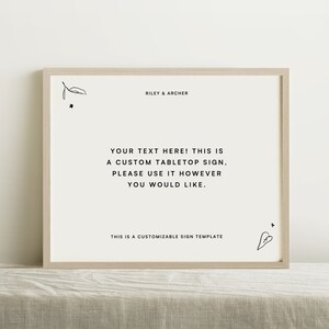 Puede incluir: Una plantilla de letrero de mesa personalizable con el texto "YOUR TEXT HERE! THIS IS A CUSTOM TABLETOP SIGN, PLEASE USE IT HOWEVER YOU WOULD LIKE." y el texto "THIS IS A CUSTOMIZABLE SIGN TEMPLATE" en la parte inferior. El letrero está en un marco de madera claro.