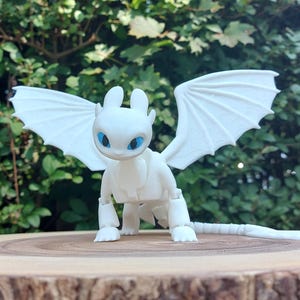 May include: White articulated dragon figurine with blue eyes and wings. The dragon is posed standing on a wooden surface.