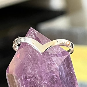 May include: A silver V-shaped ring resting on a purple amethyst crystal.
