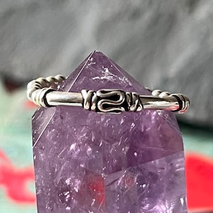May include: A silver ring with a twisted design, resting on a purple amethyst crystal.