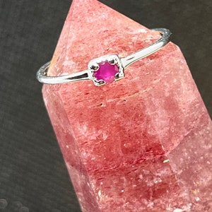 Peut inclure: Une bague en argent avec une petite pierre précieuse rose de forme carrée sertie au centre.