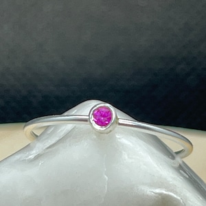 Puede incluir: Un anillo de plata sencillo con una pequeña piedra preciosa rosa brillante engastada en el centro.