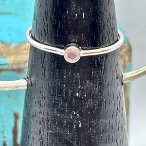 Op de afbeelding: Een delicate zilveren ring met een kleine, ronde, lichtroze edelsteen.