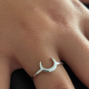 Könnte beinhalten: Ein silberner Halbmondring. Der Ring ist dünn und zart, mit einem schlichten Design.