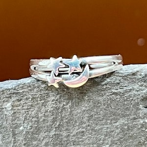 May include: A silver ring with a crescent moon and three stars design.