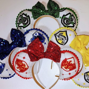 May include: Four pairs of white mouse ears with different colored bows and Hogwarts house crests. The crests are Gryffindor, Slytherin, Hufflepuff, and Ravenclaw.