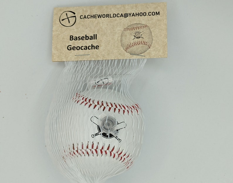 May include: A white baseball with red stitching and a black and white image of crossed bats. The baseball is in a white mesh bag and has a tag that reads "Baseball Geocache" and "CACHEWORLDCA@YAHOO.COM".