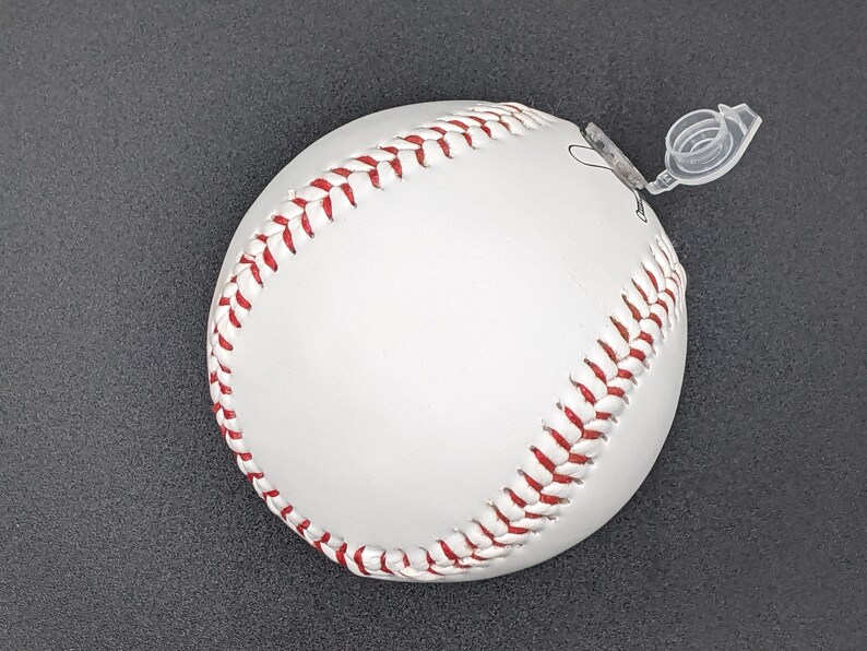 May include: White baseball with red stitching. The ball has a clear plastic tab attached to it.
