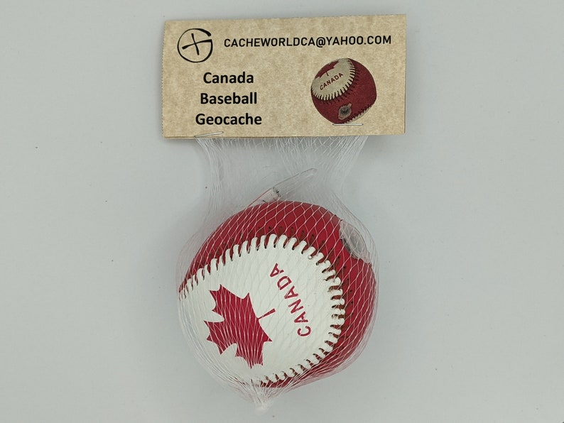 May include: A red and white baseball with a Canadian maple leaf and the word "CANADA" printed on it. The baseball is in a clear plastic bag with a brown tag that says "CACHEWORLDCA@YAHOO.COM", "Canada Baseball Geocaching".