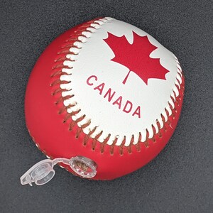 May include: A red and white baseball with a Canadian flag and the word "CANADA" printed on it. The baseball has a white valve on the side.