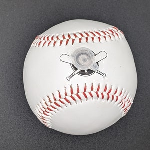 May include: White baseball with red stitching and a black and white logo of two crossed baseball bats. The baseball has a clear plastic cap on top.