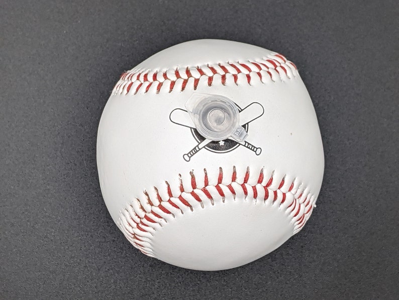 May include: White baseball with red stitching and a black and white logo of two crossed baseball bats. The baseball has a clear plastic cap on top.