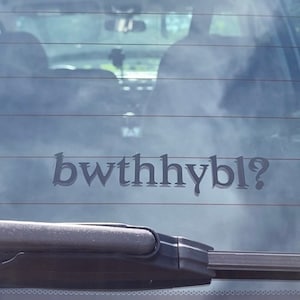 May include: A rear window of a car with a black wiper blade and a black sticker that says "bwthhybl?"